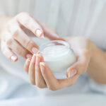 Closeup shot of hands applying moisturizer. Beauty woman holding a glass jar of skin cream. Shallow depth of field with focus on moisturizer.