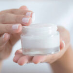 Female hand holding moisturizer in hand, horiztonal